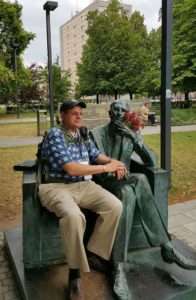 Image of Warsaw outside Polin Museum Irv sitting with statue tribute to Jan Karski, underground courier for the Polish government-in-exile, informed the West in the fall of 1942 about Nazi atrocities against Jews taking place in Poland.